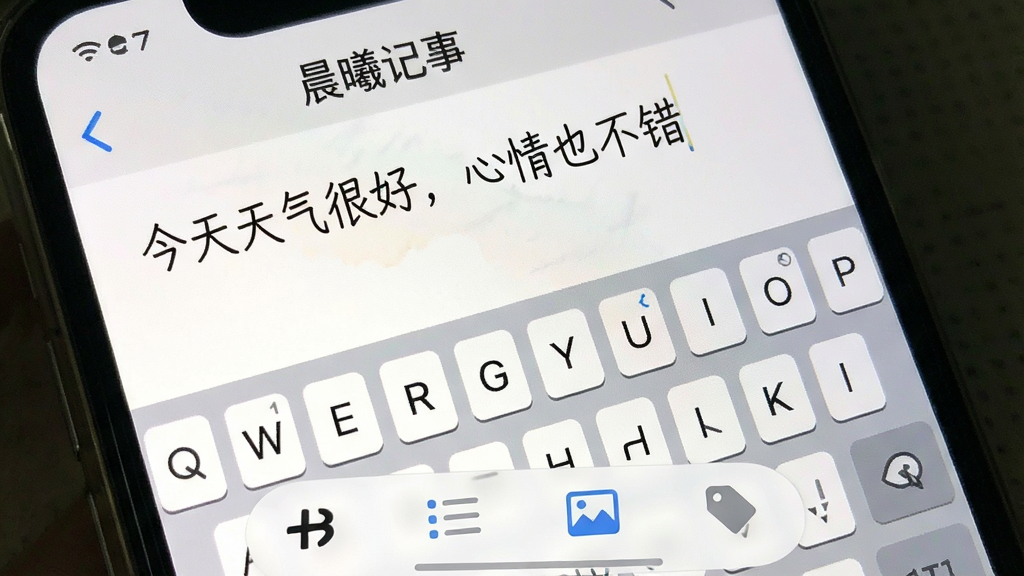 一张展示“晨曦记事”书写界面的手机截图,画面主体是手机屏幕上正在输入的日记文字,文字内容是“今天天气很好,心情也不错”,键盘弹出,底部工具栏包含加粗、列表、图片、标签等图标,整体布局紧凑合理,画质清晰,无多余元素