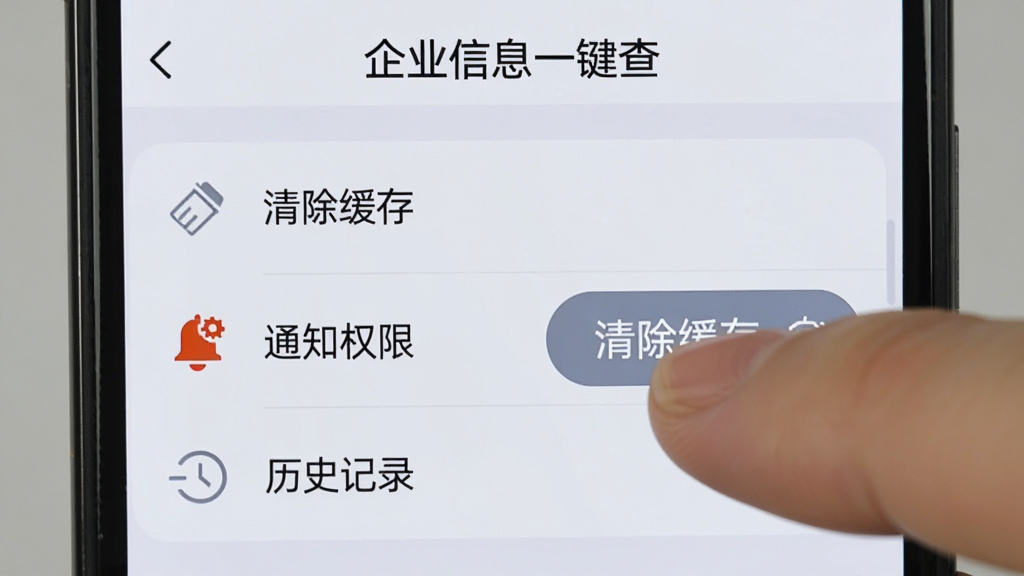 手机屏幕显示“企业信息一键查”的设置页面,页面中有“清除缓存”“通知权限”“历史记录”三个选项,其中“清除缓存”按钮被手指点击,背景是浅灰色,界面简洁,图标清晰,风格实用,画质干净无多余元素