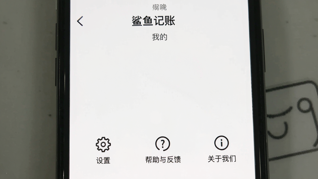 一张手机屏幕的图片,显示“鲨鱼记账”的“我的”页面,页面底部有几个功能选项,包括“设置”、“帮助与反馈”、“关于我们”,整个页面没有广告位,背景纯白,只有简单的图标和文字,画质干净无多余元素