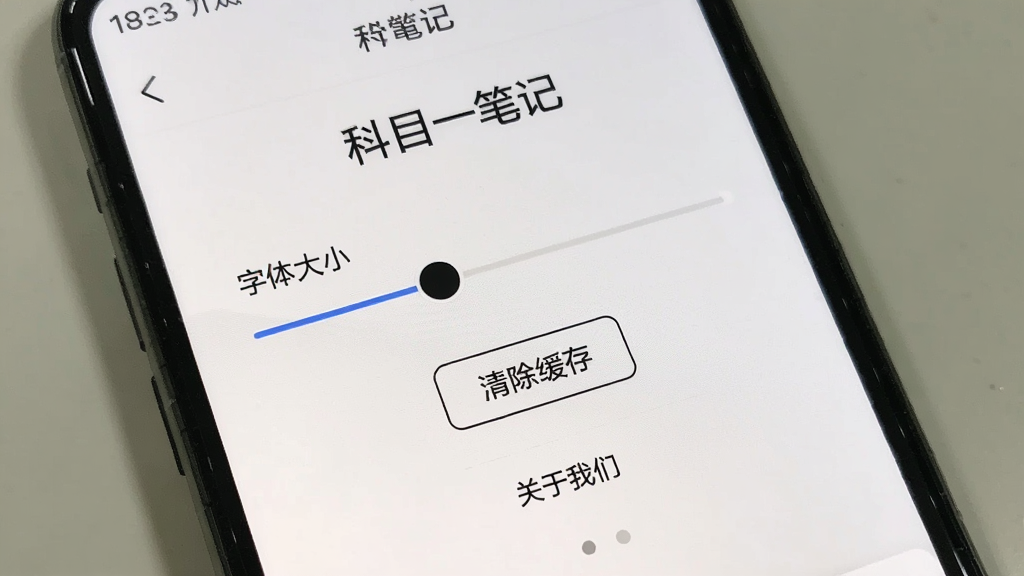 手机屏幕显示“科目一笔记”的设置页面,有字体大小滑块、清除缓存按钮和关于我们选项,背景是纯白色,图标是简单的线条风格,画质干净,无多余元素