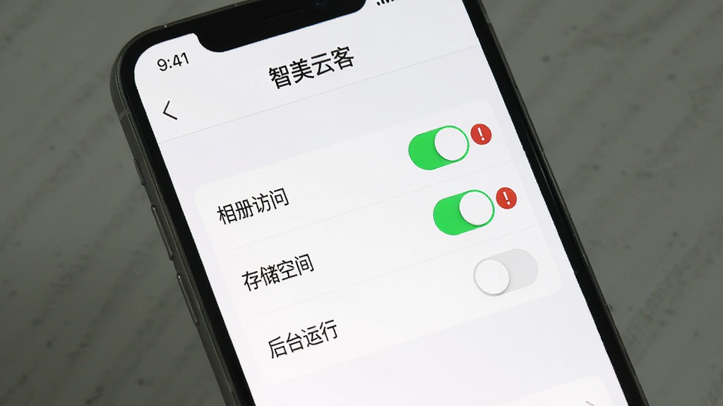 AI生图提示词:手机屏幕展示“智美云客”权限设置界面,界面上有“相册访问”“存储空间”“后台运行”三个权限开关,其中“相册访问”和“存储空间”开关显示为绿色开启状态,旁边有一个红色感叹号提示图标,背景是简洁的白色设置页面,风格清晰直观,细节明确,画质干净,无多余元素