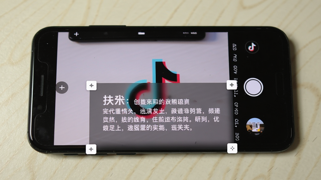 手机屏幕画面,上层是抖音拍摄界面,下层悬浮着一个半透明的提词窗口,窗口内显示白色文字,窗口边缘有调整大小的拖拽角标,手机背景为浅色桌面,整体风格写实,布局清晰,画质干净,无多余元素