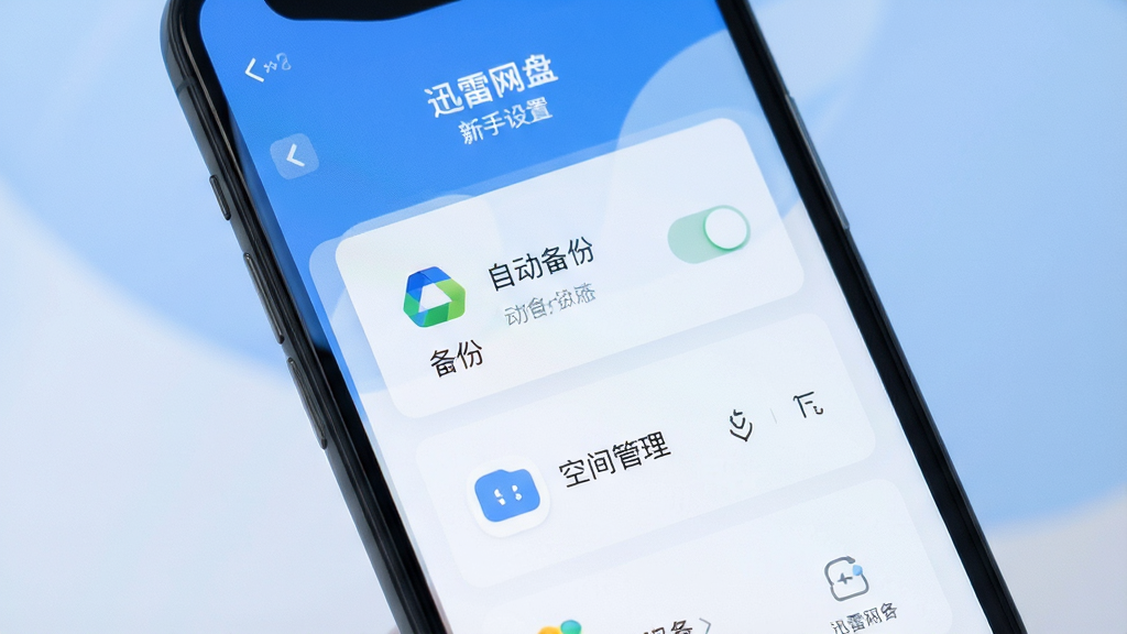 迅雷网盘 新手设置界面 手机屏幕展示自动备份开关和空间管理页面 背景为柔和的蓝白色调 图标清晰 布局合理 风格简洁友好 画质干净 无多余元素
