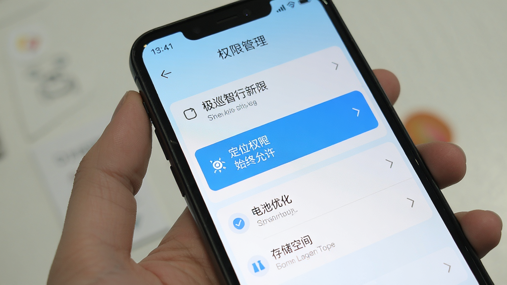 极巡智行新手设置界面展示,手机屏幕显示权限管理页面,定位权限选项被高亮标注为始终允许,下方有电池优化和存储空间的设置入口,画面风格简洁,配色以白色和浅蓝色为主,文字清晰可读,整体干净整洁,无多余元素干扰