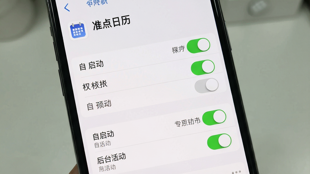 一张展示“准点日历”在手机后台权限设置界面的图片。主体是手机屏幕,显示着应用权限管理页面。布局上,顶部是“准点日历”的应用名称,中间是权限列表,下方是“自启动”和“后台活动”的开关。排版清晰,风格系统原生。细节上,开关按钮被高亮显示为开启状态,旁边有文字说明。画质清晰,干净,无多余元素。