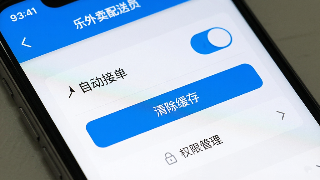 一张手机屏幕特写,展示“乐外卖配送员”App的设置页面,页面中有“自动接单”开关、“清除缓存”按钮和“权限管理”选项,界面风格扁平化,蓝白配色,画质干净无多余元素