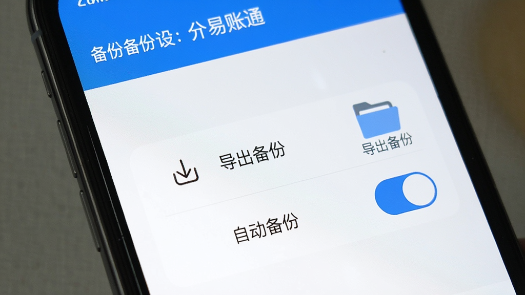 手机屏幕上显示易账通备份设置界面,有“导出备份”和“自动备份”开关,旁边有文件夹图标和提示文字,界面简洁,蓝白配色,画质清晰