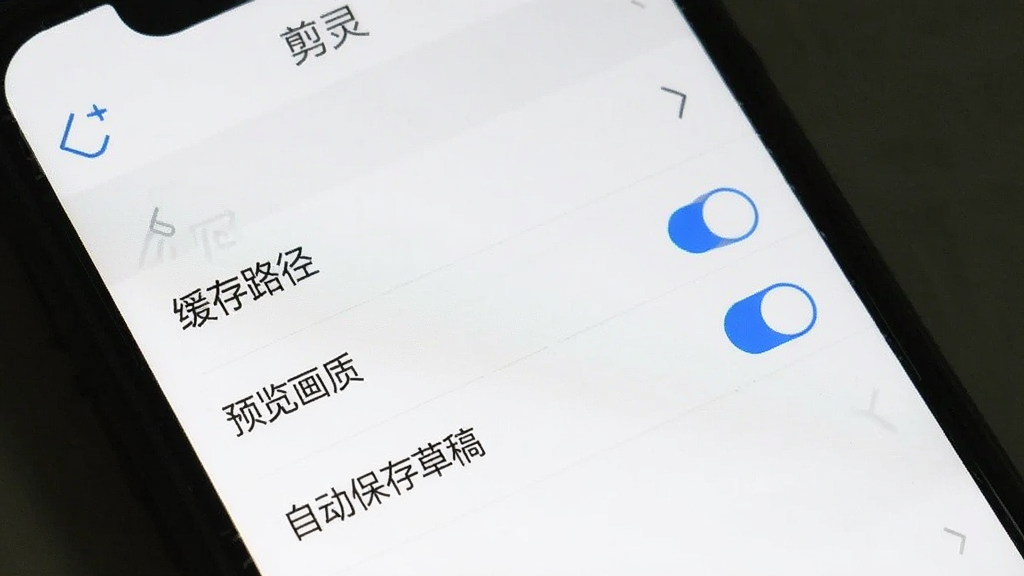 手机屏幕显示“剪灵”APP的设置界面,画面中有“缓存路径”“预览画质”“自动保存草稿”等选项开关,背景为白色,图标为蓝色线条风格,布局整齐清晰,画质干净,无多余元素。