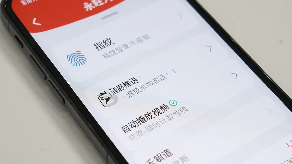 手机屏幕展示永旺App设置界面,列表中有指纹登录、消息推送、自动播放视频等选项,界面简洁,风格统一,画质清晰