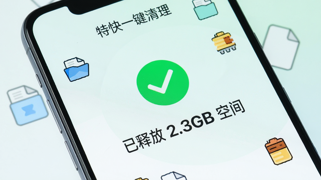 一部智能手机屏幕特写,屏幕显示“特快一键清理”App的清理完成界面,中央有一个绿色的对勾图标,下方用大号字体显示“已释放 2.3GB 空间”,背景是清爽的浅色渐变,周围散落着代表文件、缓存、内存的卡通小图标,整体风格简洁明快,画质干净无多余元素。