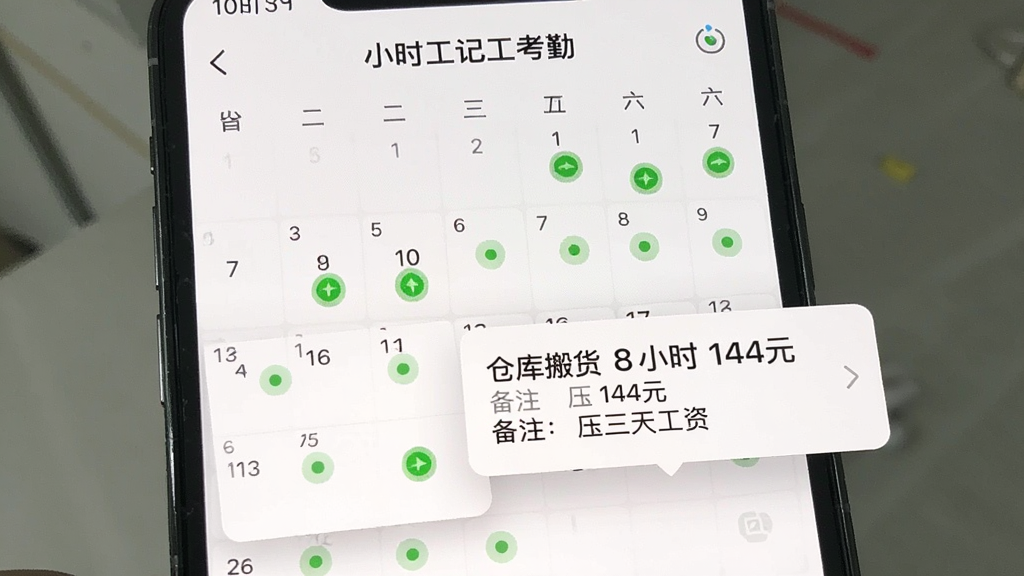 手机屏幕显示“小时工记工考勤”的日历页面,月历上部分日期有绿色圆点标记,点击某日期弹出详情卡片显示“仓库搬货 8小时 144元 备注:压三天工资”,界面清爽,文字清晰,画质干净无多余元素