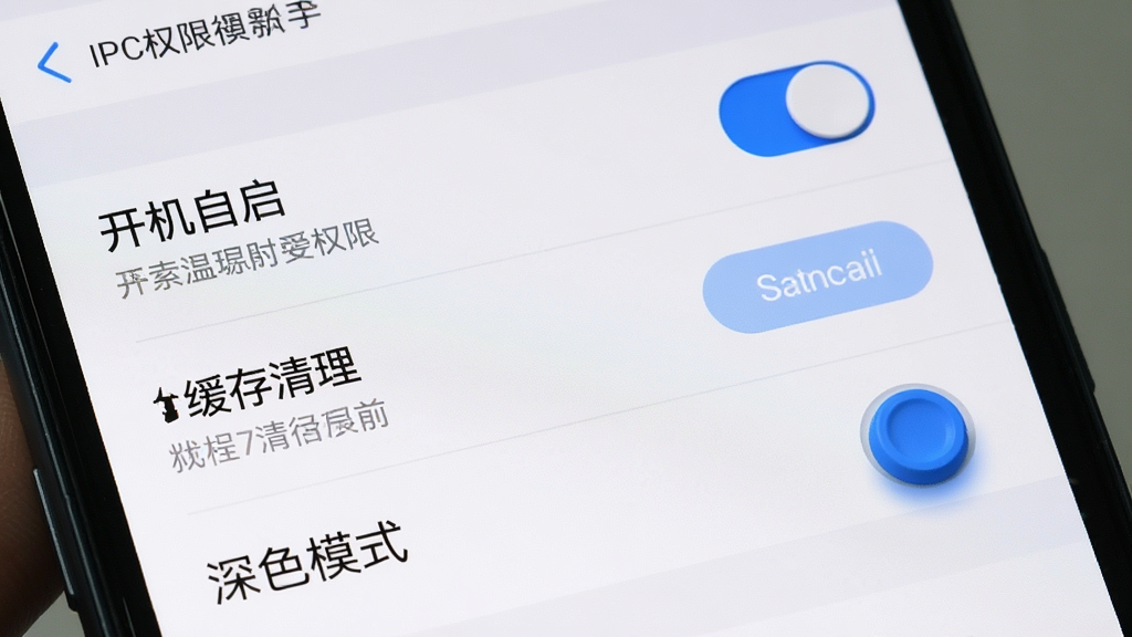 AIPC新手设置界面截图,主体为手机屏幕显示权限管理页面,页面中有“开机自启”开关、“缓存清理”按钮和“深色模式”选项;布局采用列表形式,每个选项旁有说明文字;排版清晰;风格为系统原生设置风,色彩以白、蓝、灰为主;细节上开关有立体感,按钮有按压反馈效果;画质干净,无多余装饰,用于教程配图。